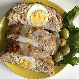 Preparation of minced meat rolls. As a stuffing boiled egg. Slices of the finished roll are on a plate with olives and greens.