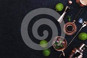 Preparation Moscow Mule cocktail with ginger beer, vodka, lime and ice. Copper bar tools. Black bar counter background. Top view.