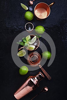 Preparation Moscow Mule cocktail with ginger beer, vodka, lime and ice. Copper bar tools. Black bar counter background. Top view.