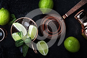 Preparation Moscow Mule cocktail with ginger beer, vodka, lime and ice. Copper bar tools. Black bar counter background. Top view.