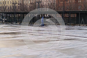 Preparation for outdoor sport activity: male worker pour water at ice rink, skating rink for hockey