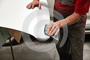 Preparation for painting a car element using emery sponge by a service technician leveling out before applying a primer after photo