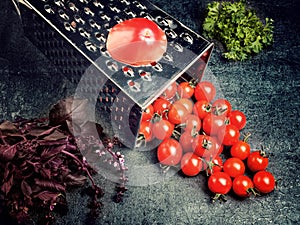 Preparation recipe tomato juice. Large tomato and old grater down to small grape cherry tomatoes on retro vintage rustic gray ston