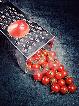 Preparation recipe tomato juice. Large tomato and old grater down to small grape cherry tomatoes on retro vintage rustic gray ston