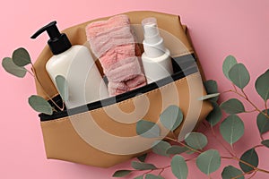 Preparation for spa. Compact toiletry bag with different cosmetic products and eucalyptus on pink background, flat lay