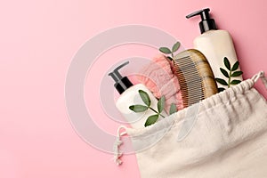 Preparation for spa. Compact toiletry bag with different cosmetic products and twigs on pink background, flat lay. Space for text