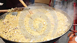 Preparation of traditional Catalan pasta fideua with shrimps and mussels in large paellera on street festival. Spanish