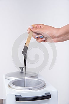 Preparation of wax for shugaring. Closeup of depilation wax on wooden stick holding female hand on white background