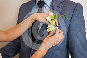 Preparations the groom for the wedding. Bride puts on boutonniere on groom`s jacket. Romantic wedding moment