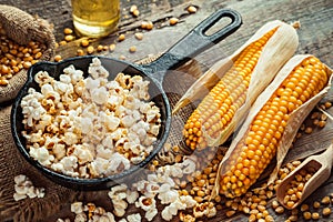 Prepared popcorn in frying pan, corn seeds and corncobs