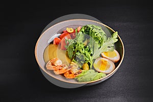 Prepared shrimps or prawns with boiled eggs, avocado, fresh tomatoes and arugula in a plate over black background