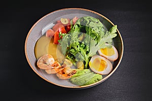 Prepared shrimps or prawns with boiled eggs, avocado, fresh tomatoes and arugula in a plate over black background