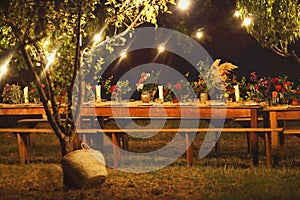 Prepared table for a rustic outdoor dinner at night with wineglasses, flowers and lamps
