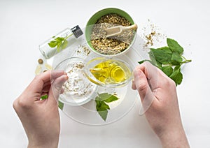 Preparing an alternative medicine, herbal extract: white background, hands hold a jar of oil over a bowl with white essence, and