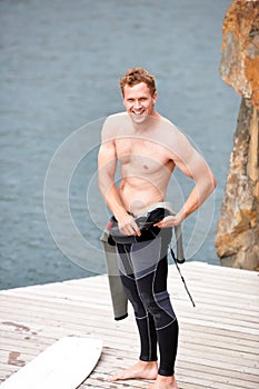 Preparing for an awesome day. Young man putting on his wetsuit before engaging in some watersports.