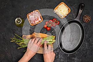 Preparing bacon wrapped asparagus on dark table.  Woman cooking asparagus. Ingredients for cooking on black background