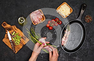 Preparing bacon wrapped asparagus on dark table.  Woman cooking asparagus. Ingredients for cooking on black background