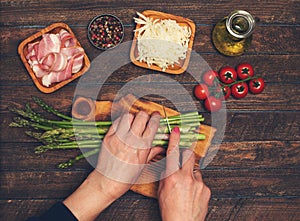 Preparing bacon wrapped asparagus on dark table.  Woman cooking asparagus. Ingredients for cooking on black background