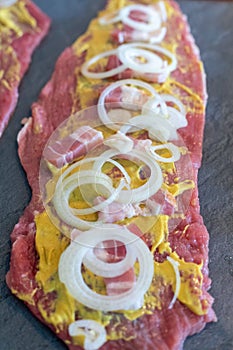 Preparing beef rouladen, fresh raw meat coated with mustard and onions