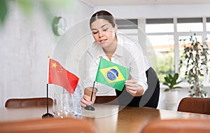 Preparing for business negotiations - woman sets small flags of countries of China and Brazil on table