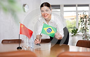 Preparing for business negotiations - woman sets small flags of countries of China and Brazil on table