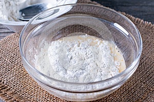 Preparing a dough/batter for crepes or pancakes with wheat flour in glass bowl, milk, eggs and oil