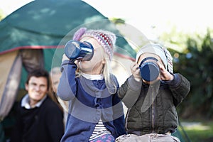 Preparing for an energetic days camping. Loving parents watching their children drinking from mugs while out camping.