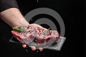 Preparing fresh beef or pork on a dark background. Chef salts steak in a freeze motion with rosemary and spices. Long banner