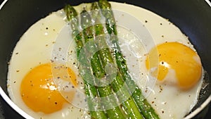 Preparing fried eggs with fresh asparagus on frying pan