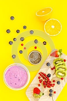 Preparing healthy fruit smoothie. Acai smoothie bowl near cutting board with fresh fruits, berries, chia seeds on yellow