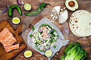 Preparing healthy lunch snacks. Fish tacos with grilled salmon, red onion, fresh salad leaves and avocado cilantro sauce