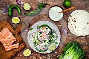 Preparing healthy lunch snacks. Fish tacos with grilled salmon, red onion, fresh salad leaves and avocado cilantro sauce