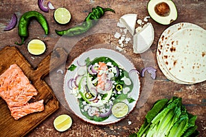 Preparing healthy lunch snacks. Fish tacos with grilled salmon, red onion, fresh salad leaves and avocado cilantro sauce