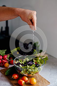 preparing healthy salad in kitchen, adding salt to the bowl