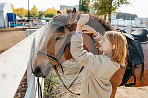 Preparing her horse for the ride, ginger girl putting on bridle on horse