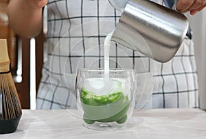 Preparing iced green tea matcha latte, pouring the fresh milk into a glass with ice