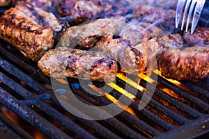 Preparing meat rolls called mici or mititei on barbecue. close up of grill with burning fire with flame and smoke