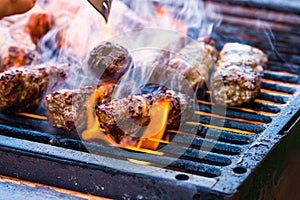 Preparing meat rolls called mici or mititei on barbecue. close up of grill with burning fire with flame and smoke