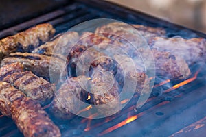 Preparing meat rolls called mici or mititei on barbecue. close up of grill with burning fire with flame and smoke