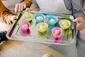 Preparing muffins for baking. Dough divided into silicone colourful cups lying on metal baking tray. Close-up of women