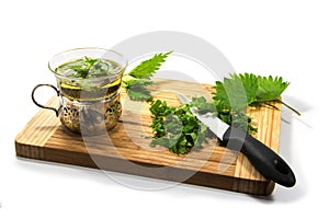 Preparing nettle tea, leaves, knife and teacup on a wooden cutting board on a white background