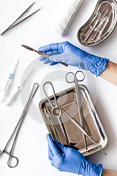 Preparing for plastic surgery. Doctor`s hands takes scalpel on white background with surgical tools top view