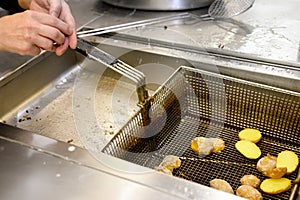 Preparing potatoes in deep fryer with boiling oil.