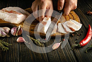 Preparing a snack from pork lard by the hands of a man. Knife in the hand of a cook for cutting lard into small pieces