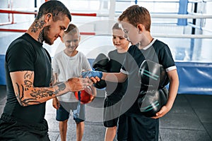 Preparing for the sparring. Young tattooed coach teaching the kids boxing techniques