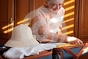 Preparing suitcase for summer vacation trip. Elderly woman checking accessories and stuff in luggage on the bed at home before