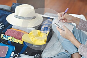 Preparing suitcase for summer vacation trip. Young woman checking accessories and stuff in luggage on the bed at home.