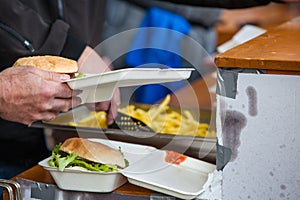 Preparing take away meal with freshly cooked burger and french fries on outdoors kitchen at street music festival