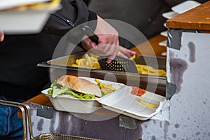 Preparing take away meal portion with freshly cooked burger and french fries on outdoors kitchen at street music festival