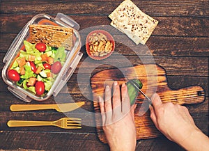 Preparing takeaway meal for children. School lunch box with salad, salmon, avocado  and nuts on rustic wooden background. Healthy